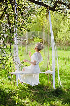Young bride with blond hair in white negligee using perfume on a rope swing