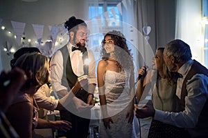 A young bride and groom with other guests dancing and singing on a wedding reception.