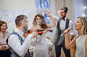 A young bride, groom and other guests dancing and singing on a wedding reception.