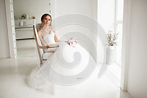 Young bride in a luxury dress holding a bouquet of flowers in bright white studio. Wedding fashion concept.