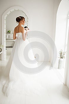 Young bride in a luxury dress holding a bouquet of flowers in bright white studio. Wedding fashion concept.