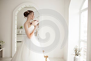 Young bride in a luxury dress holding a bouquet of flowers in bright white studio. Wedding fashion concept.