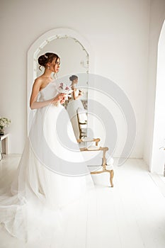 Young bride in a luxury dress holding a bouquet of flowers in bright white studio. Wedding fashion concept.