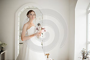 Young bride in a luxury dress holding a bouquet of flowers in bright white studio. Wedding fashion concept.