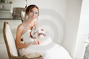 Young bride in a luxury dress holding a bouquet of flowers in bright white studio. Wedding fashion concept.