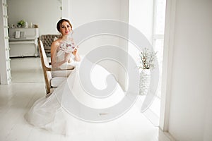 Young bride in a luxury dress holding a bouquet of flowers in bright white studio. Wedding fashion concept.