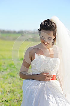 Young bride outdoor portrait in white dress against green field
