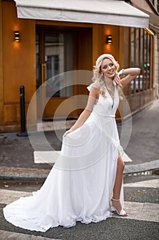 Young bride with pearl tiara, in wedding dress walking in Paris. Girl hold long attire with hand and smile softly.