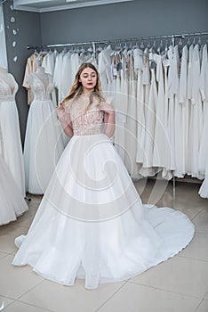 The young bride tries on an elegant wedding dress and pose in the salon