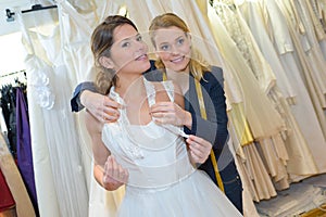 Young bride trying on wedding dress with assistant