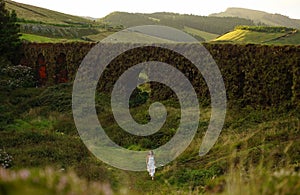 Young bride in white dress going barefoot without shoes in green field between bushes. Small woman in green fairy tale