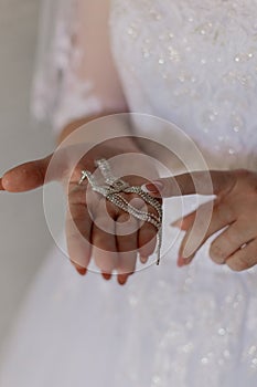 A young bride in a white dress holds earrings in her hands in order to put them on for marriage registration.