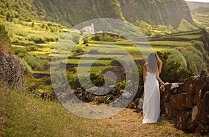 Young bride in white wedding dress. View from behind. Romantic background of beautiful idyllic valley and ocean coast