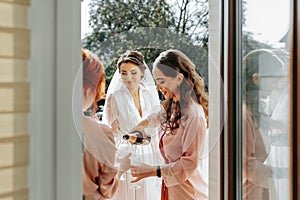 Young bridesmaids are having fun and smiling in pink silk robes drinking champagne at the bride's gazebo.