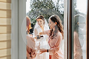 Young bridesmaids are having fun and smiling in pink silk robes drinking champagne at the bride's gazebo.