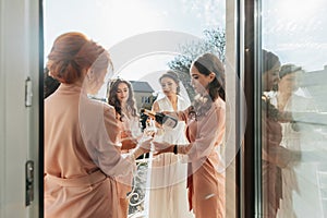 Young bridesmaids are having fun and smiling in pink silk robes drinking champagne at the bride's gazebo.