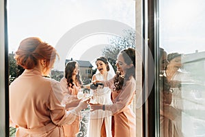 Young bridesmaids are having fun and smiling in pink silk robes drinking champagne at the bride's gazebo.