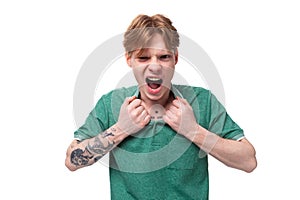 a young bright ginger man with a tattoo on his arm, dressed in a green short-sleeved T-shirt, screams in anger