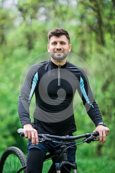 Young bright man on mountain bike in green forest