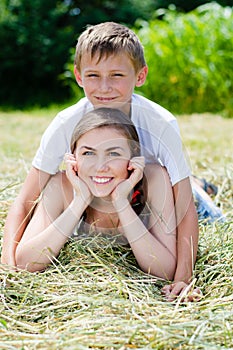 Young brother and elder sister or mother & son smiling together on dry hay on summer day