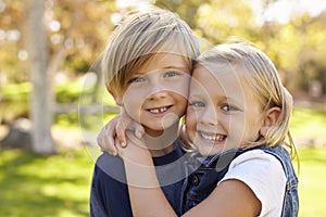 Young brother and sister embracing in a park look to camera