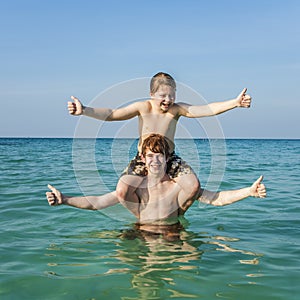 Young brothers are enjoying the clear warm water at the beautiful beach and playing pickaback