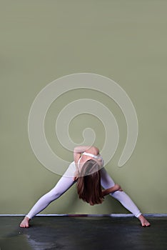 Young brown-haired girl in oigi pose - Parivrata prasarita padottanasana - Bend with legs wide apart with twisting.