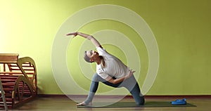 A young brown-haired woman is training in a fitness studio, stretching the lateral muscles of the body
