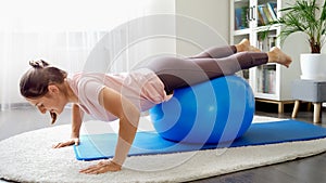 Young bruentte woman rolling on fitness ball at home and doing push-ups