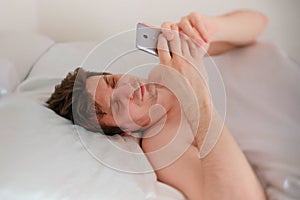 Young brunet handsome man wakes up, and check the time on his mobile phone.