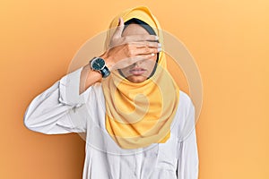 Young brunette arab woman wearing traditional islamic hijab scarf covering eyes with hand, looking serious and sad