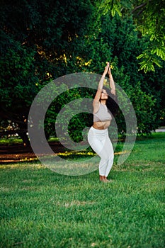 Young brunette asian woman practicing yoga during workout in park