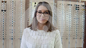 A young brunette with blue eyes in a cozy white sweater in an optics store holds glasses in front of the camera and then