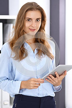 Young brunette business woman looks like a student girl at work in office. Girl standing straight with tablet pc