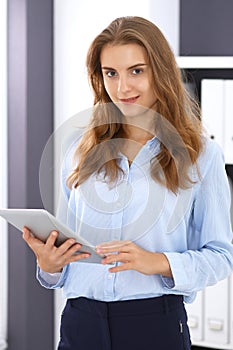 Young brunette business woman looks like a student girl at work in office. Girl standing straight with tablet pc