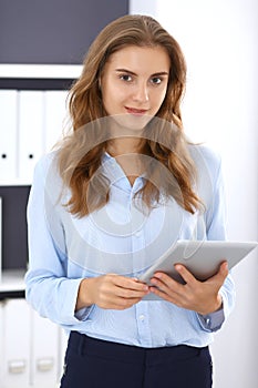 Young brunette business woman looks like a student girl at work in office. Girl standing straight with tablet pc