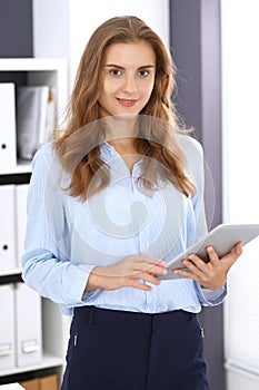 Young brunette business woman looks like a student girl at work in office. Girl standing straight with tablet pc