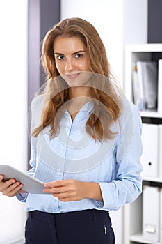 Young brunette business woman looks like a student girl at work in office. Girl standing straight with tablet pc