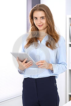 Young brunette business woman looks like a student girl at work in office. Girl standing straight with tablet pc