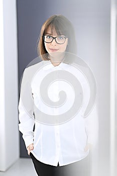 Young brunette business woman looks like a student girl working in office. Caucasian girl standing straight