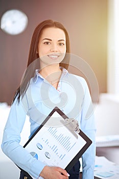 Young brunette business woman looks like a student girl working in office. Hispanic or latin american girl happy at work