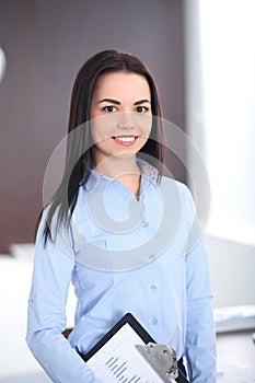 Young brunette business woman looks like a student girl working in office. Hispanic or latin american girl happy at work