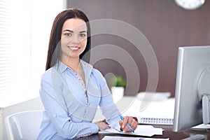 Young brunette business woman looks like a student girl working in office. Hispanic or latin american girl happy at work