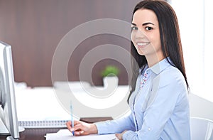 Young brunette business woman looks like a student girl working in office. Hispanic or latin american girl happy at work