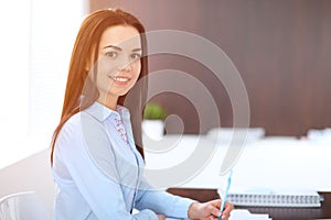 Young brunette business woman looks like a student girl working in office. Hispanic or latin american girl sitting at