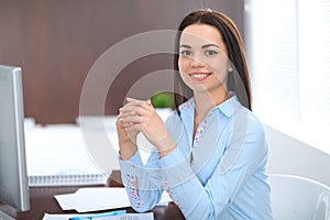 Young brunette business woman looks like a student girl working in office. Hispanic or latin american girl sitting at