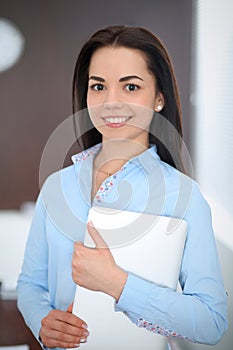 Young brunette business woman looks like a student girl working in office. Hispanic or latin american girl standing
