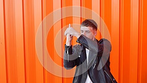 Young brunette caucasian man playing with an imaginary gun on an orange background, close-up, slow motion