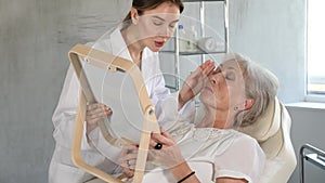 Young brunette cosmetologist consulting old gray haired lady in front of mirror at exam room of aesthetic center