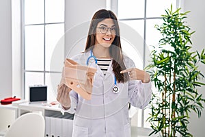 Young brunette doctor woman holding cervical neck collar pointing finger to one self smiling happy and proud
